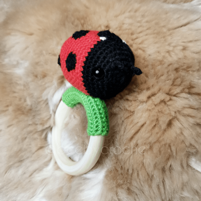 Vauvan virkattu helistin, leppäkerttu, musta pää, punainen ruumis, mustat täplät, joita seitsemän kappaletta. Puinen rengas