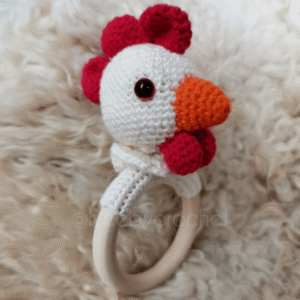 Virkattu vauvan helistin, valkoinen kanan pää, punaiset heltat ja oranssi nokka. Puinen rengas