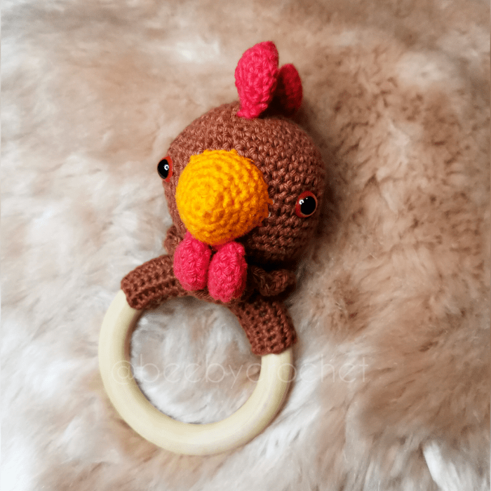 Virkattu vauvan helistin, ruskea kanan pää, punaiset heltat ja oranssi nokka. Puinen rengas